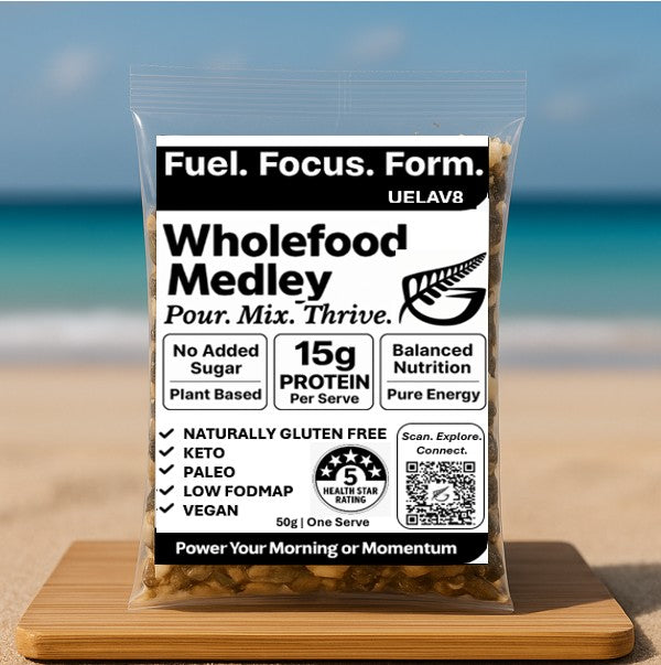 UELAV8 Wholefood Medley single-serve sachet displayed on a wooden board at the beach – clean NZ-made high protein, low carb nut and seed blend.